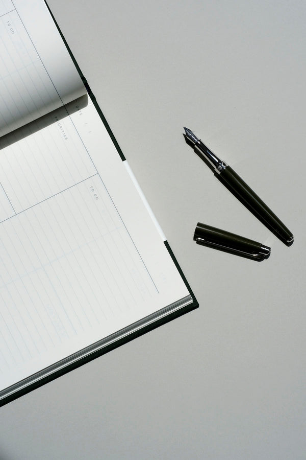Open Caran d’Ache Léman Slim fountain pen next to a Work Journal notebook on a gray background.