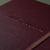 Wypukły napis Bullet Journal na froncie śliwkowego notatnika.