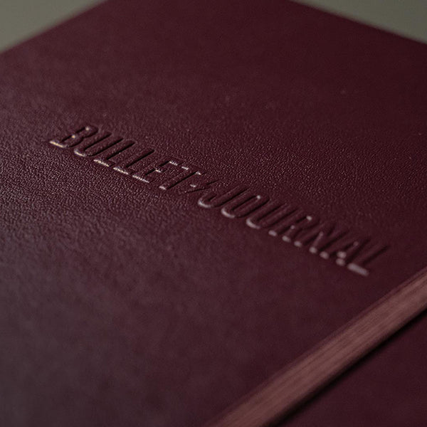 Wypukły napis Bullet Journal na froncie śliwkowego notatnika.