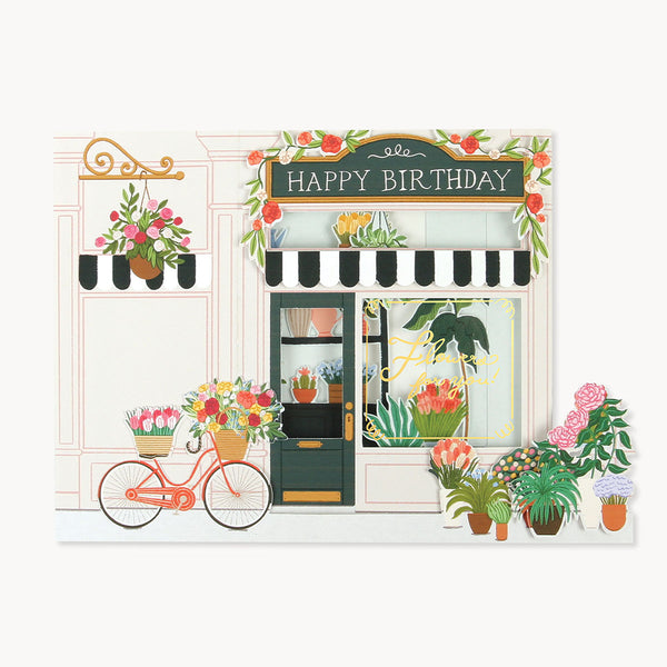 A folded greeting card featuring flowers, a bicycle, and the words "Happy Birthday" on a signboard.