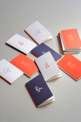 Pocket-sized notebooks from the Luna collection with a moon motif in orange, navy, and light grey.