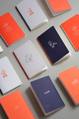 Pocket-sized notebooks from the Luna collection with a moon motif in orange, navy, and light grey.