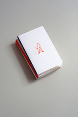 A small light grey notebook with a orange illustration inspired by the Moon.