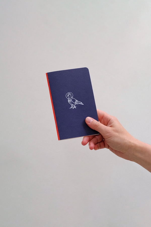 A small navy notebook with a white illustration, held in a hand.