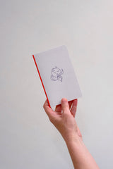 A small light grey notebook with a navy illustration, held in a hand.