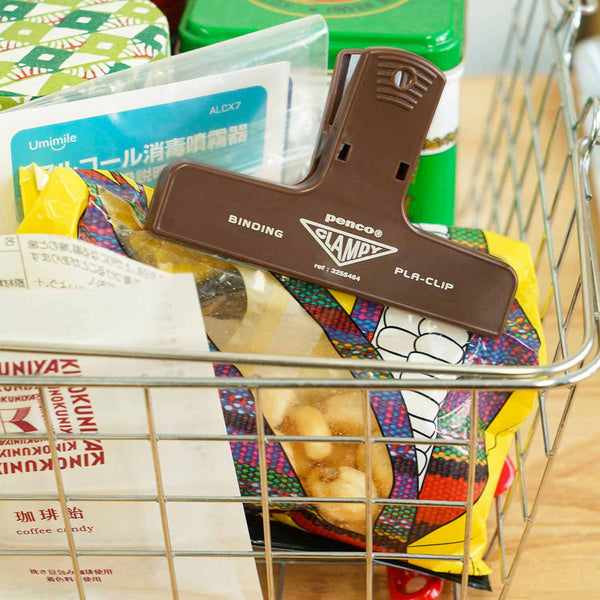 A brown plastic paper clip with a yellow logo, used to seal a snack bag.