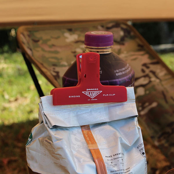 A red plastic paper clip with a white logo, used to seal a snack bag.