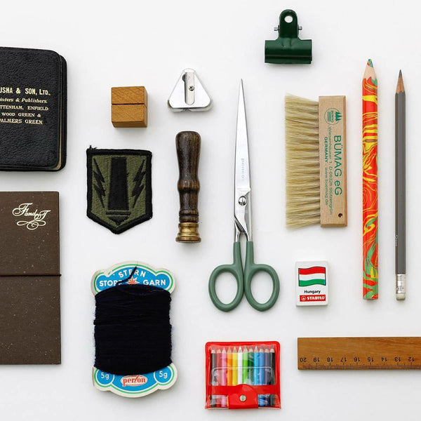 Steel scissors with green handles and the Penco brand name engraved on them, alongside other office supplies.